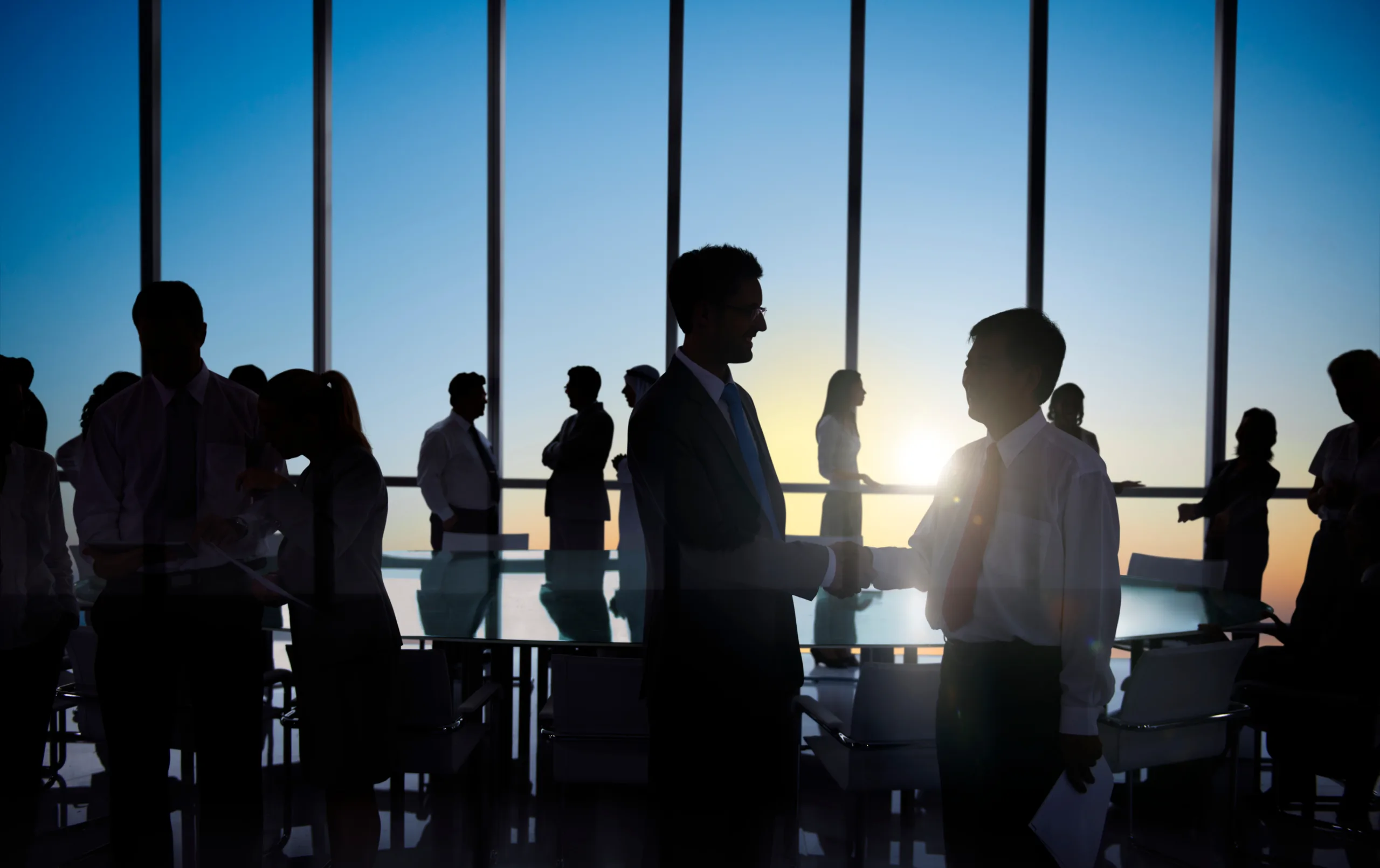 People in a big room while 2 men shaking hands cutting a procure iq deal
