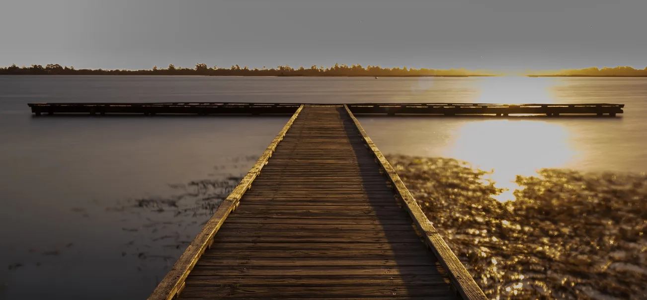 a wooden dock that extendes into the water at sunset
